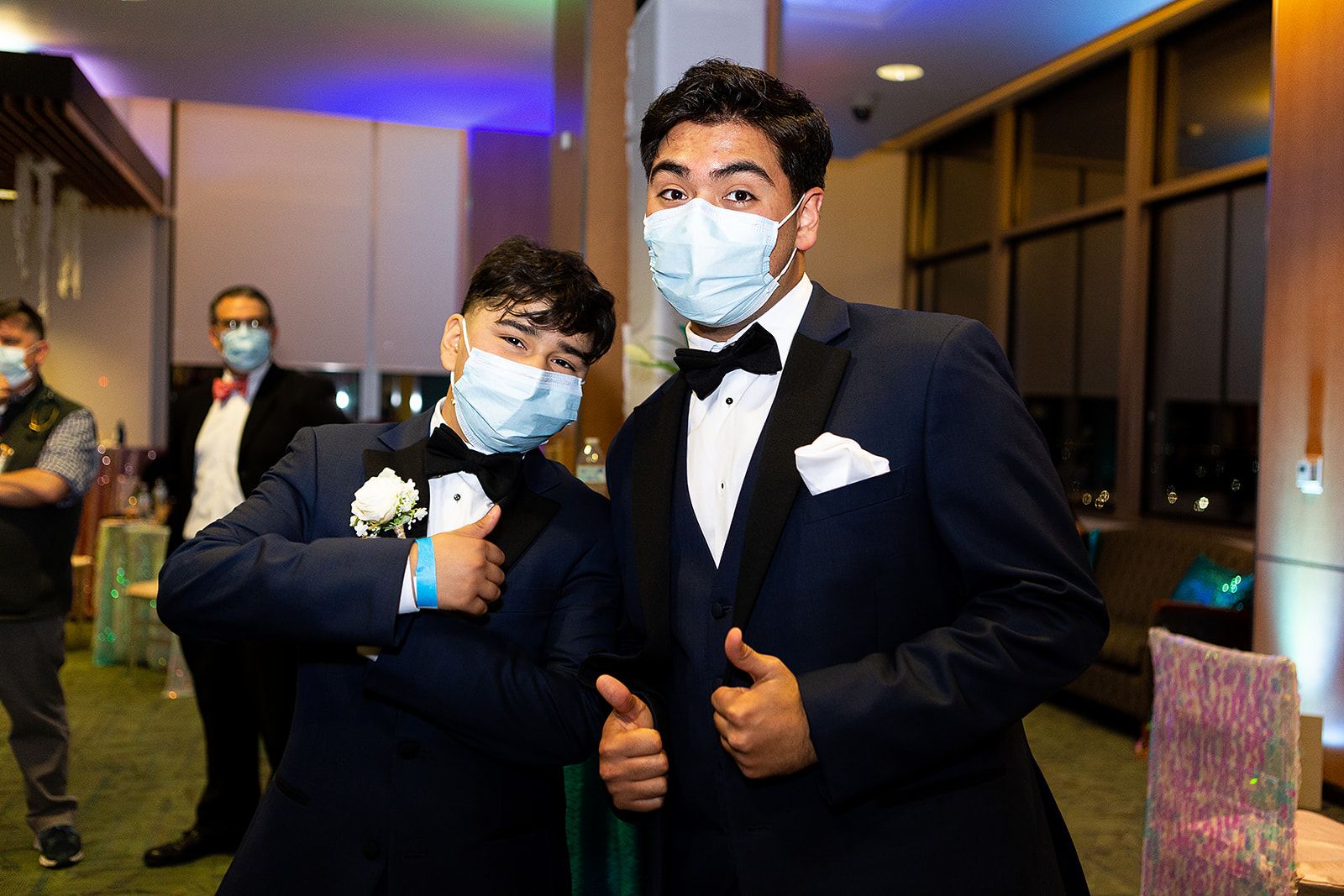 Two young men wearing black tuxedos giving a thumbs up.