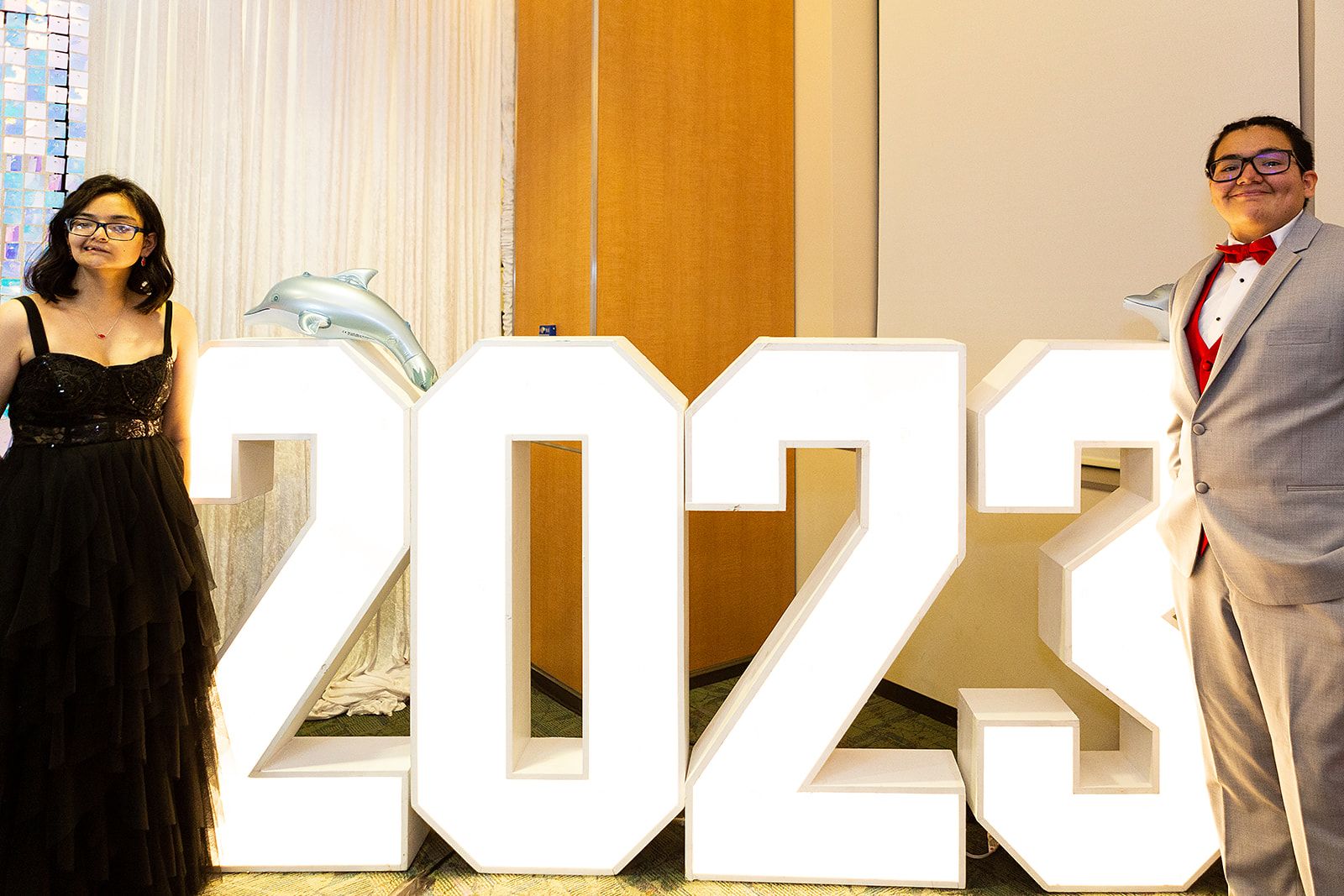 Two prom attendees stand next to large block numbers that say 2023.