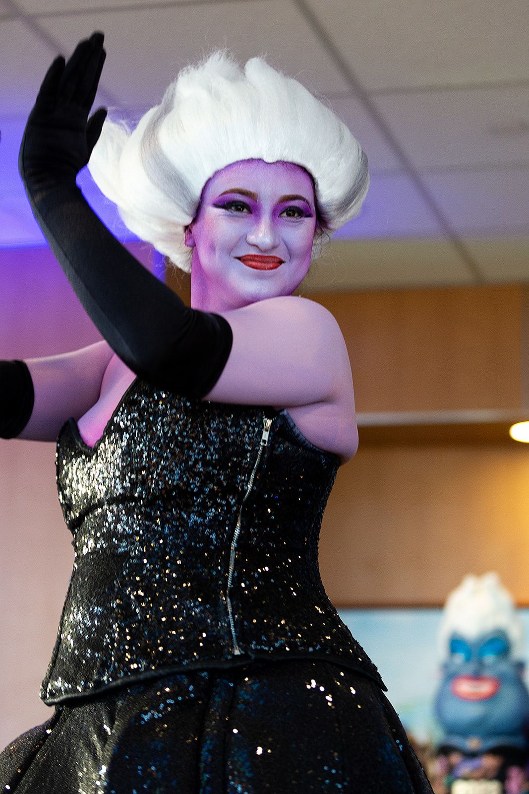 A performer dressed as Ursula from the Little Mermaid. She is covered in purple body paint and wearing a white wig and long black gloves.