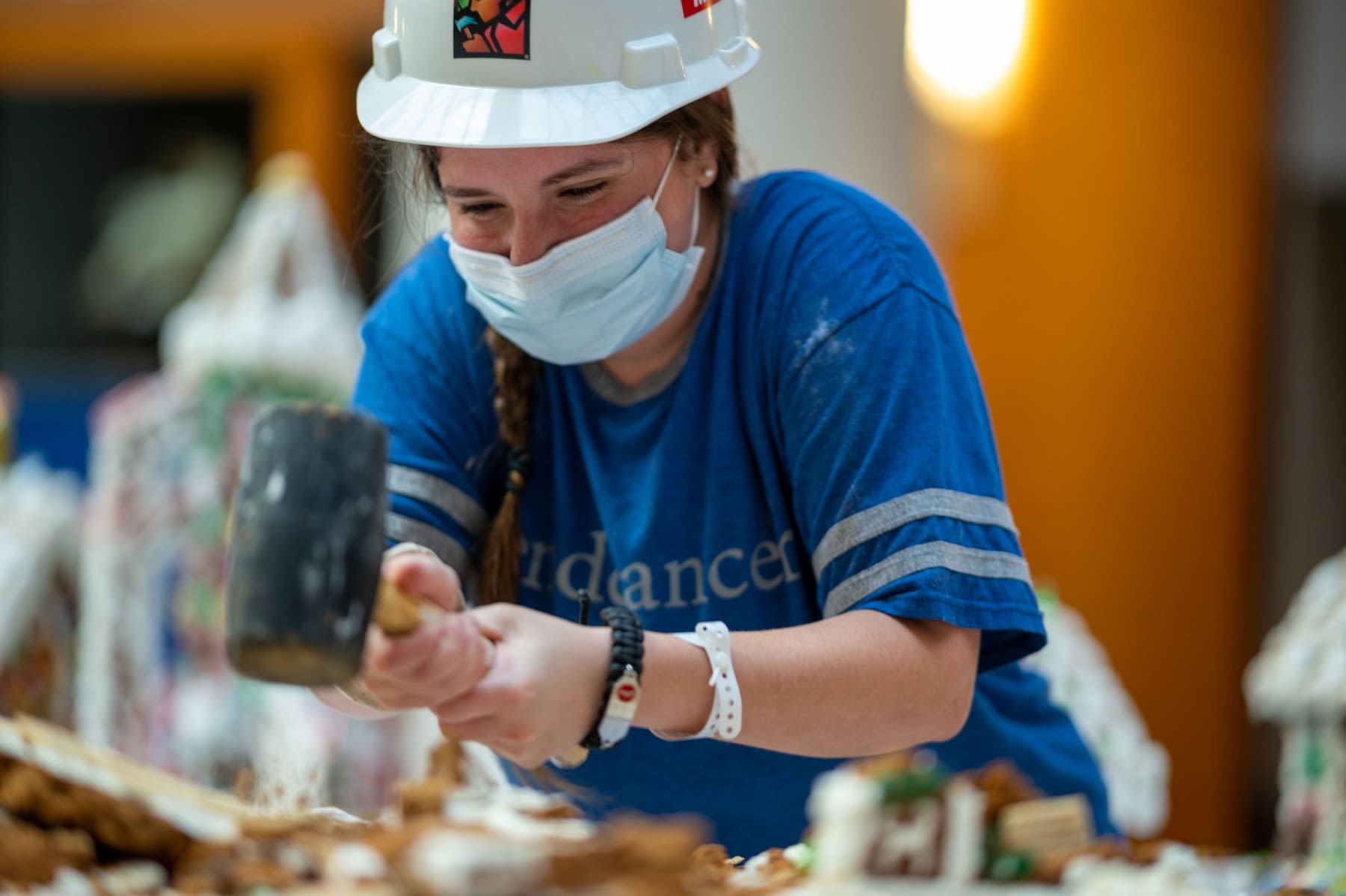 A person in a blue shirt wearing a surgical face mask using a mallet.