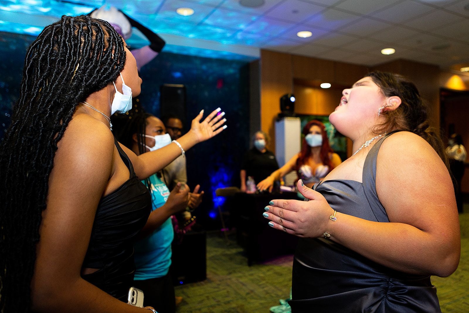 Prom attendees singing along. They are wearing sleeveless black and gray gowns.