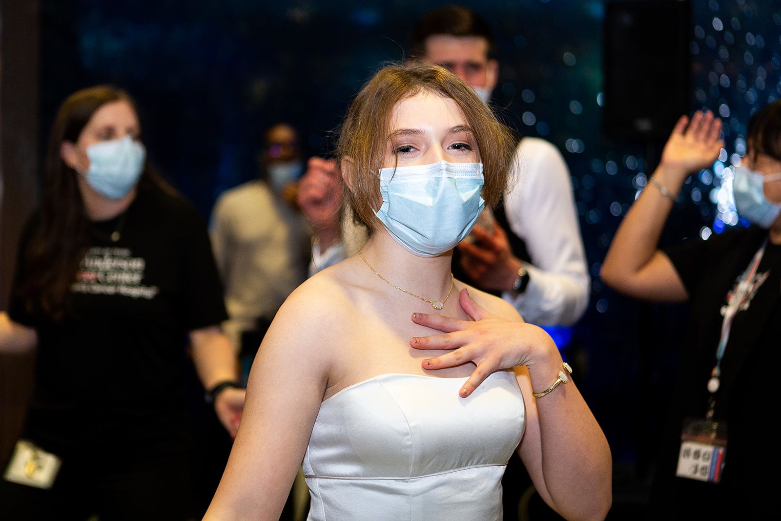A prom attendee wearing a white strapless dress and a dainty gold necklace dancing.