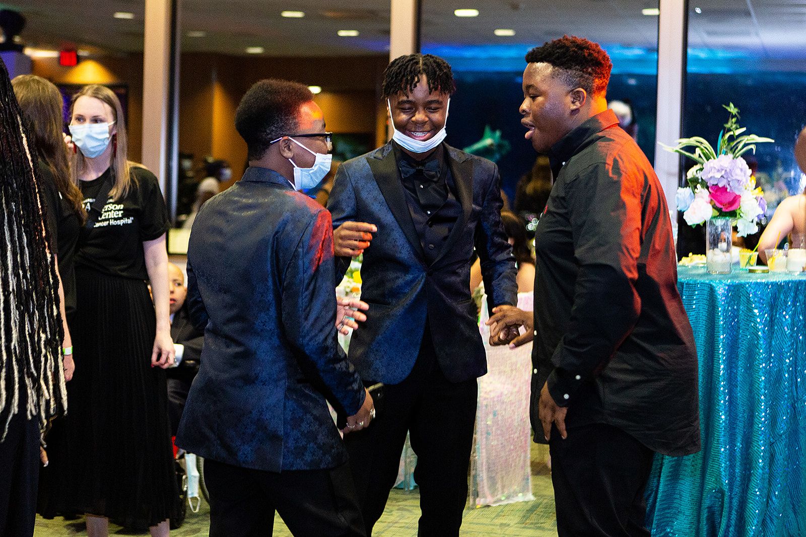 A group of young men wearing black and navy suits smile and talk at the prom.