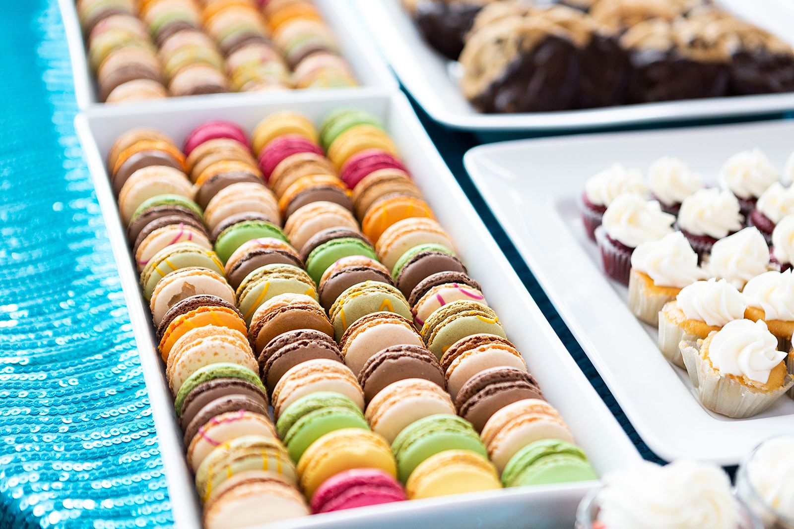 Brown, light green, orange, fuschia, and peach colored macarons in a white rectangular tray.