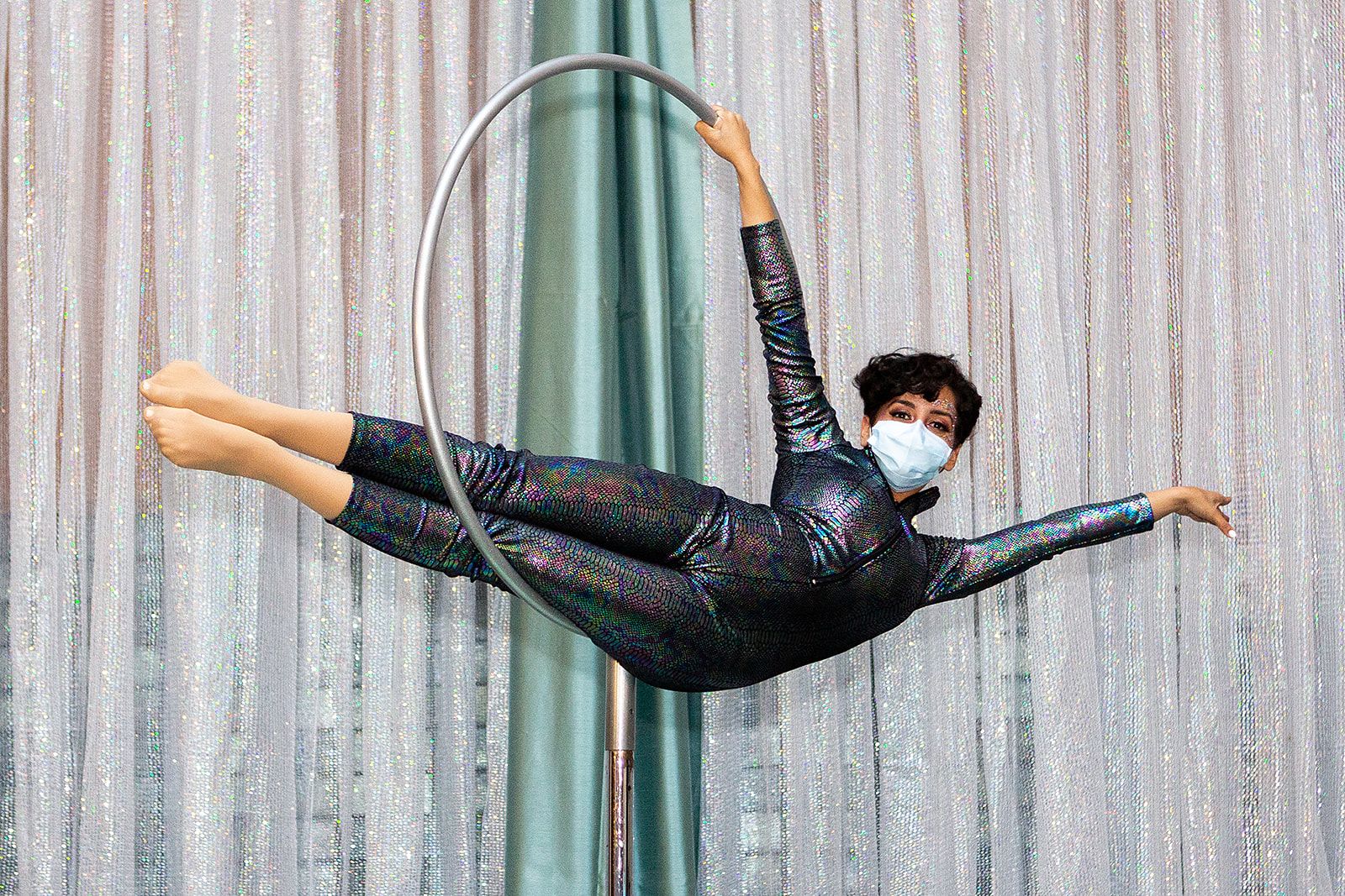 An acrobatic performer laying horizontal in a silver hoop that is suspended in the air.
