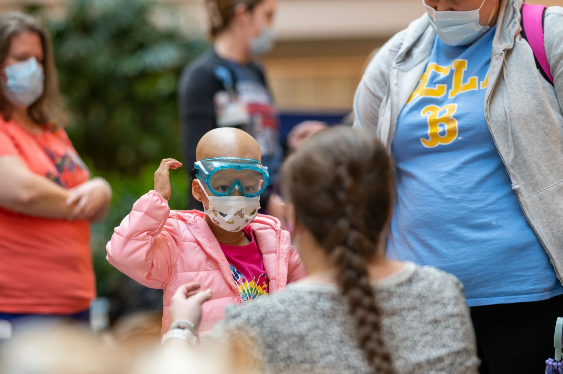 A young child wearing safety goggles, a surgical face mask and a pink, puffy coat.