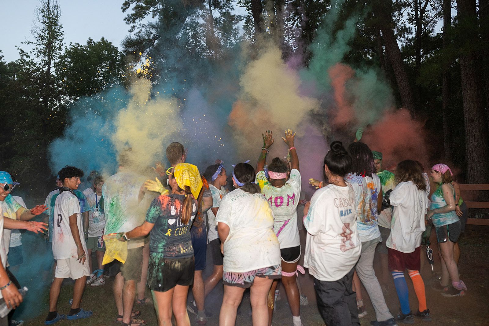 Several people in white shirts in front of plumes of colored powder going up into the air.