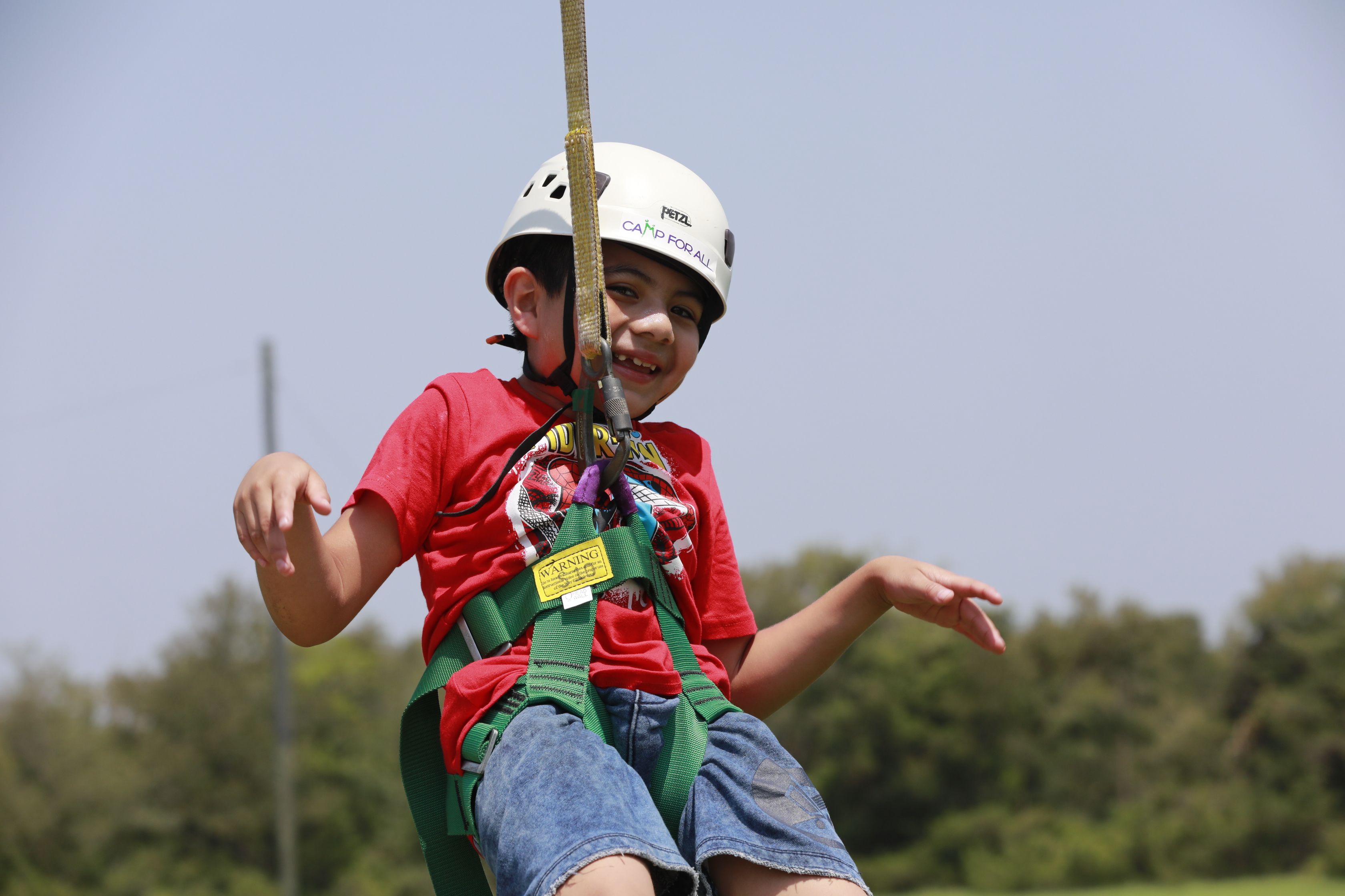 A smiling child wearing a helmet as he sits in a zip line harness