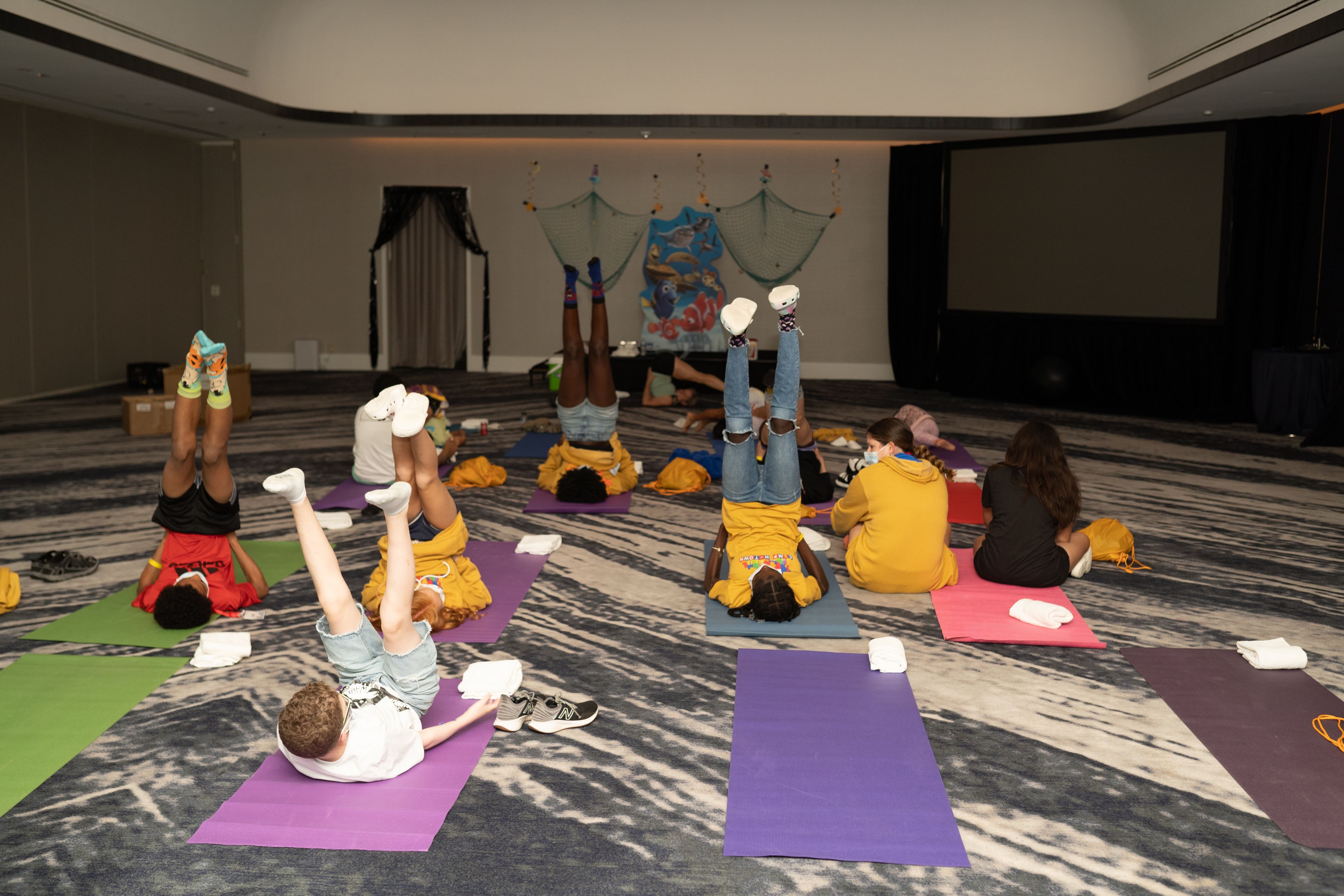 People lying on colorful yoga mats in a large indoor space, raising their legs during a group exercise