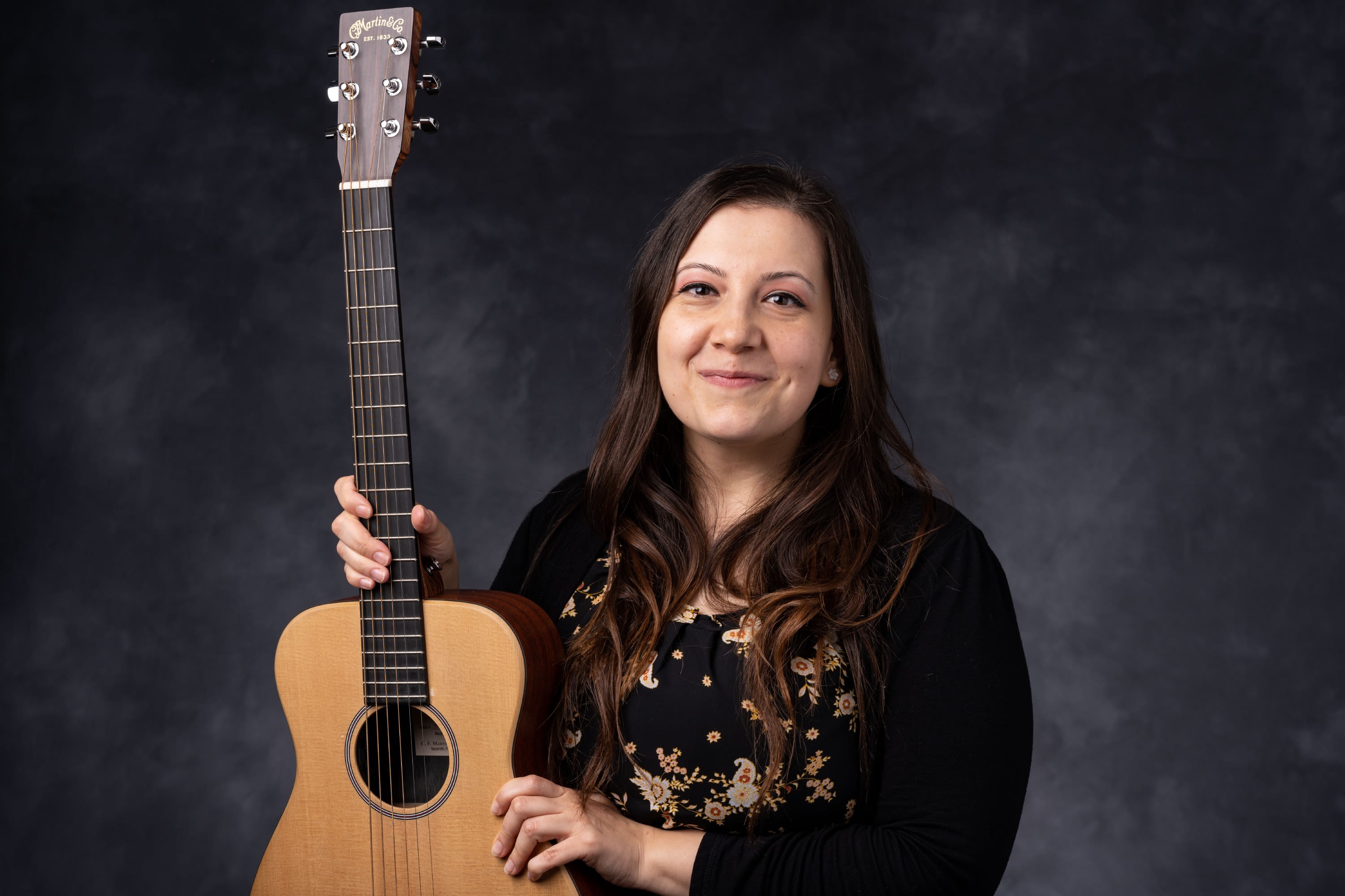 A headshot of Melissa Melo. She is holding a guitar.