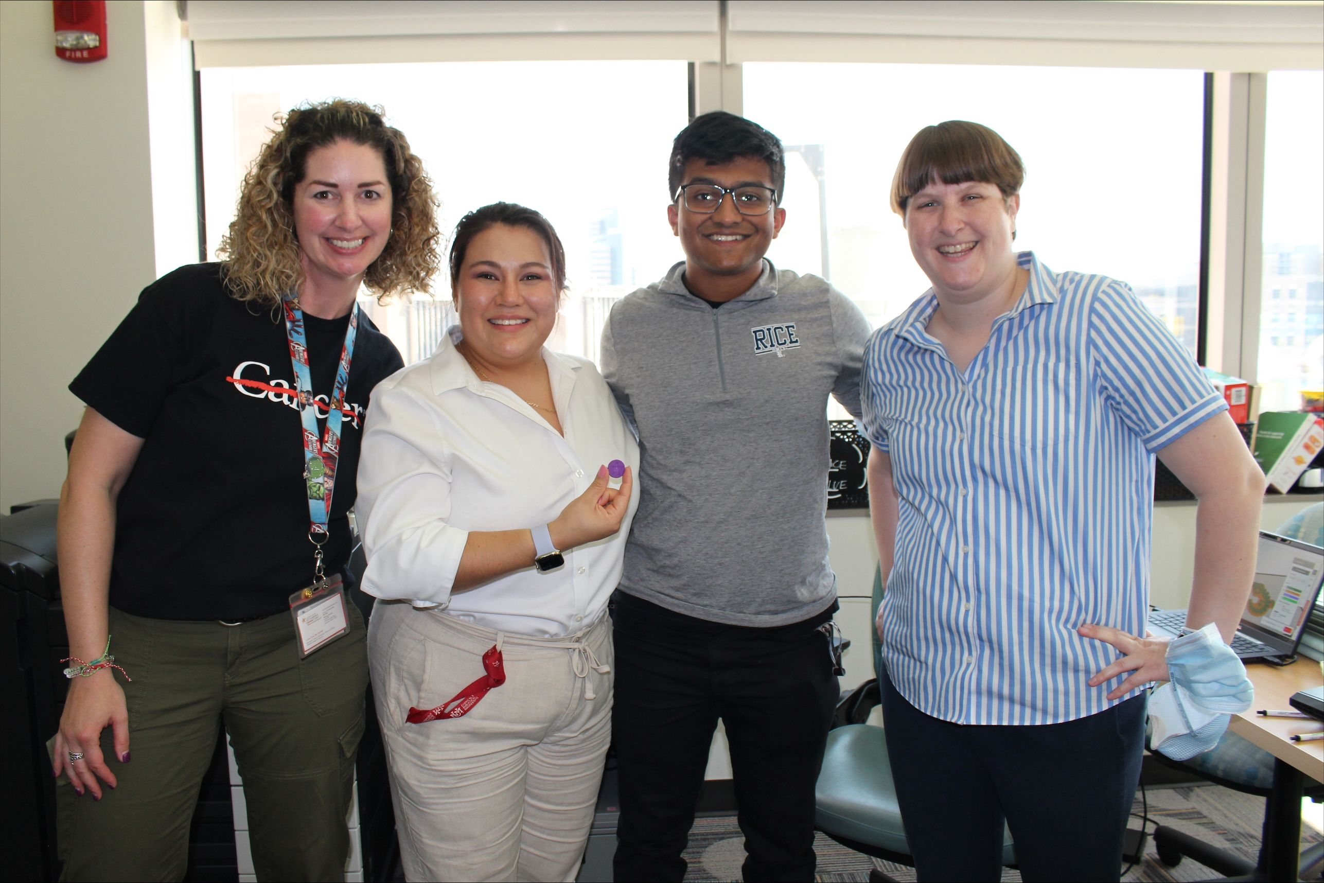 Four people standing indoors in front of bright windows, smiling at the camera.