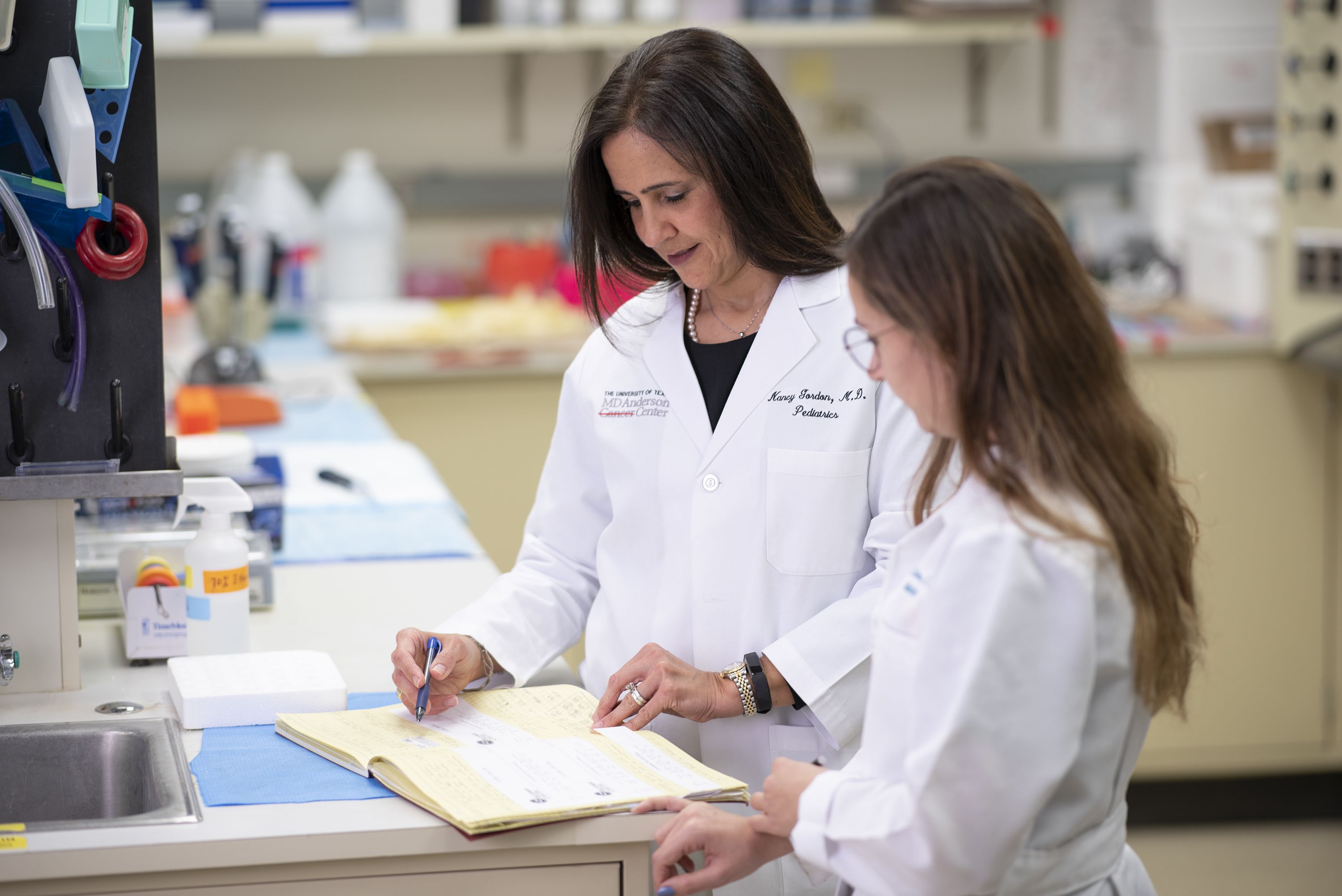 Two women wearing lab coats looking at a notebook in a laboratory.