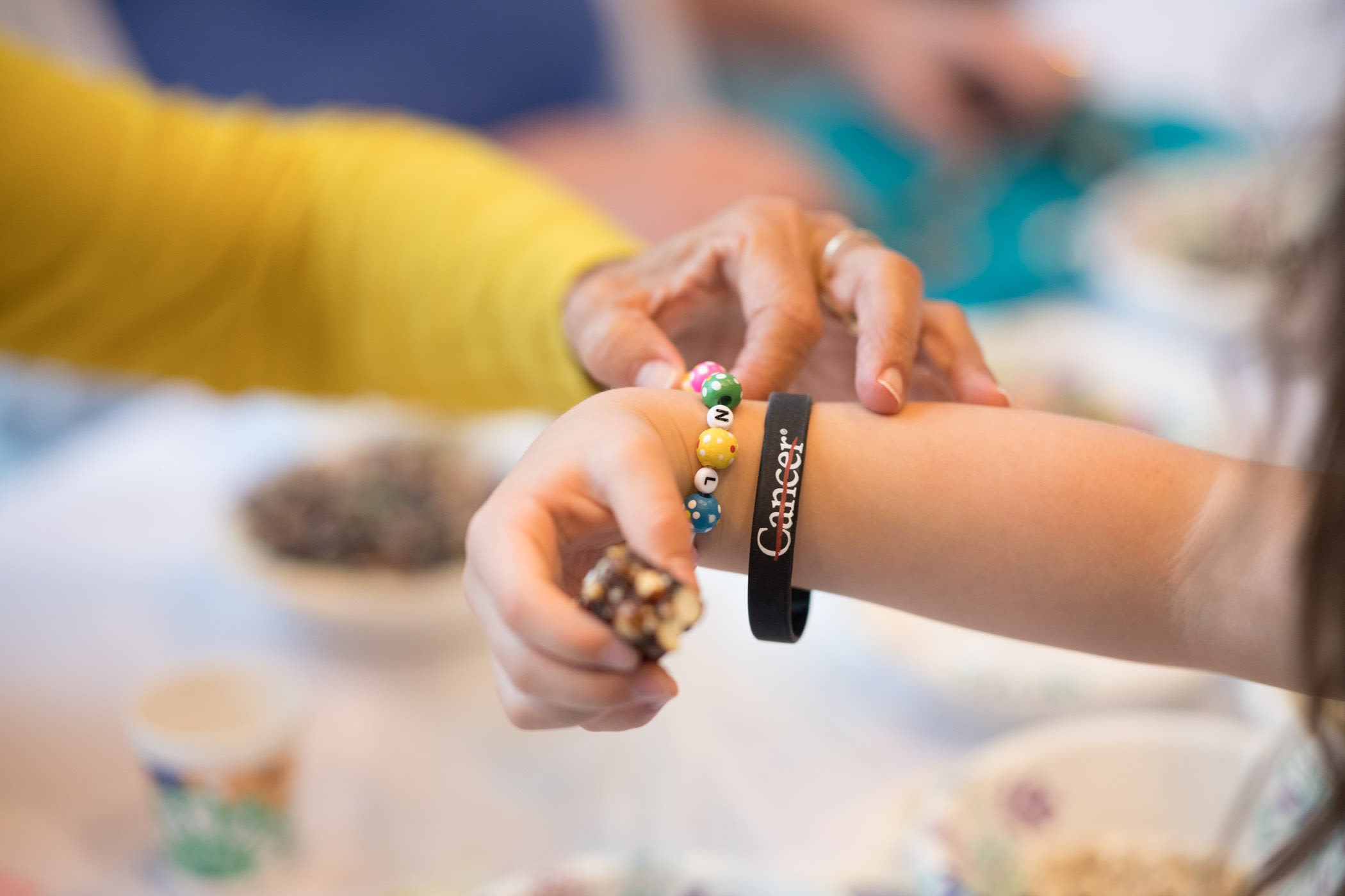 A wrist with a multicolor beaded bracelet and a black rubber bracelet with the MD Anderson Cancer Strikethrough logo on it.