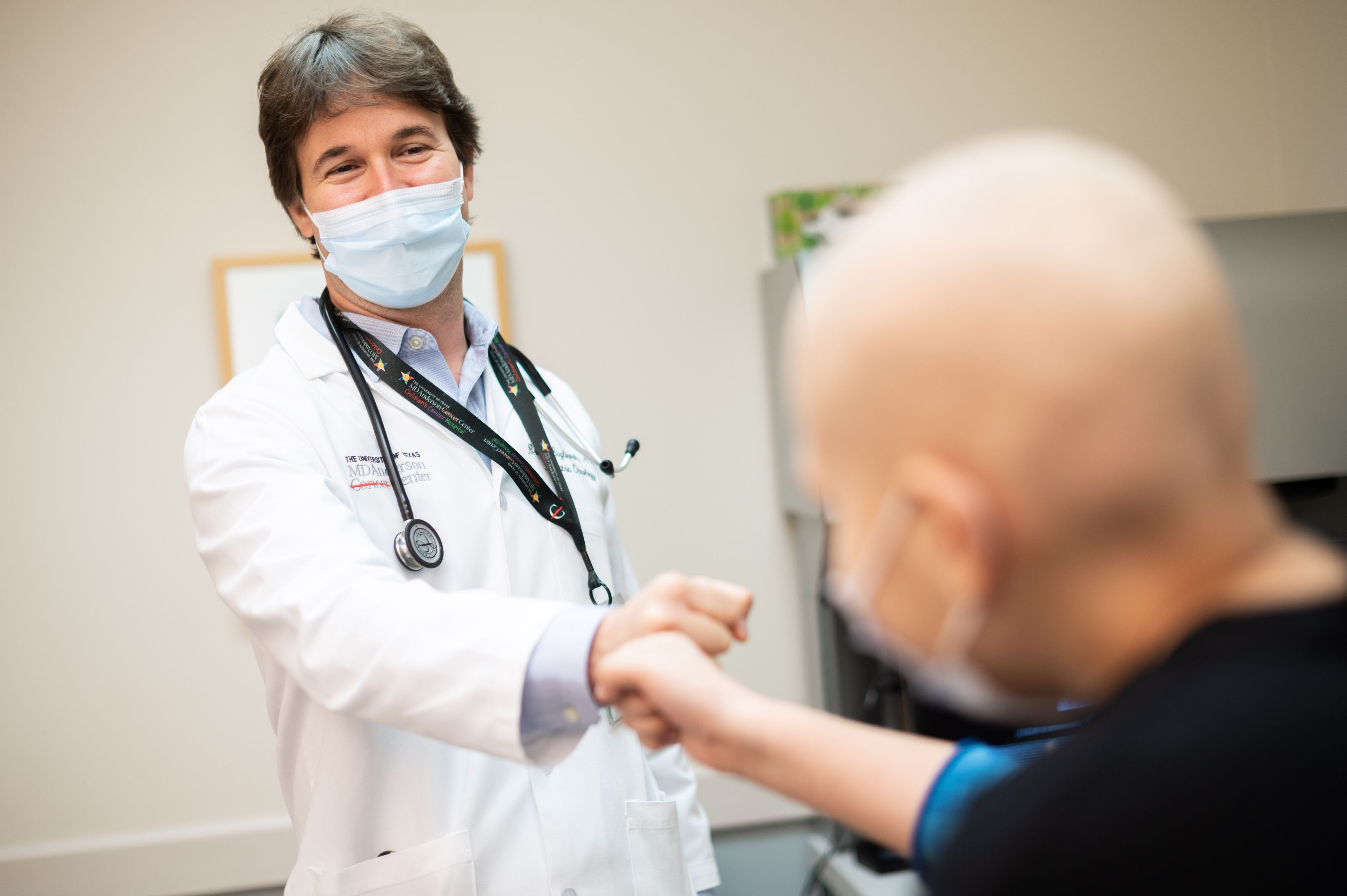 Dr. Branko Cuglievan wearing a surgical face mask with a stethoscope around his neck shaking hands with a patient.