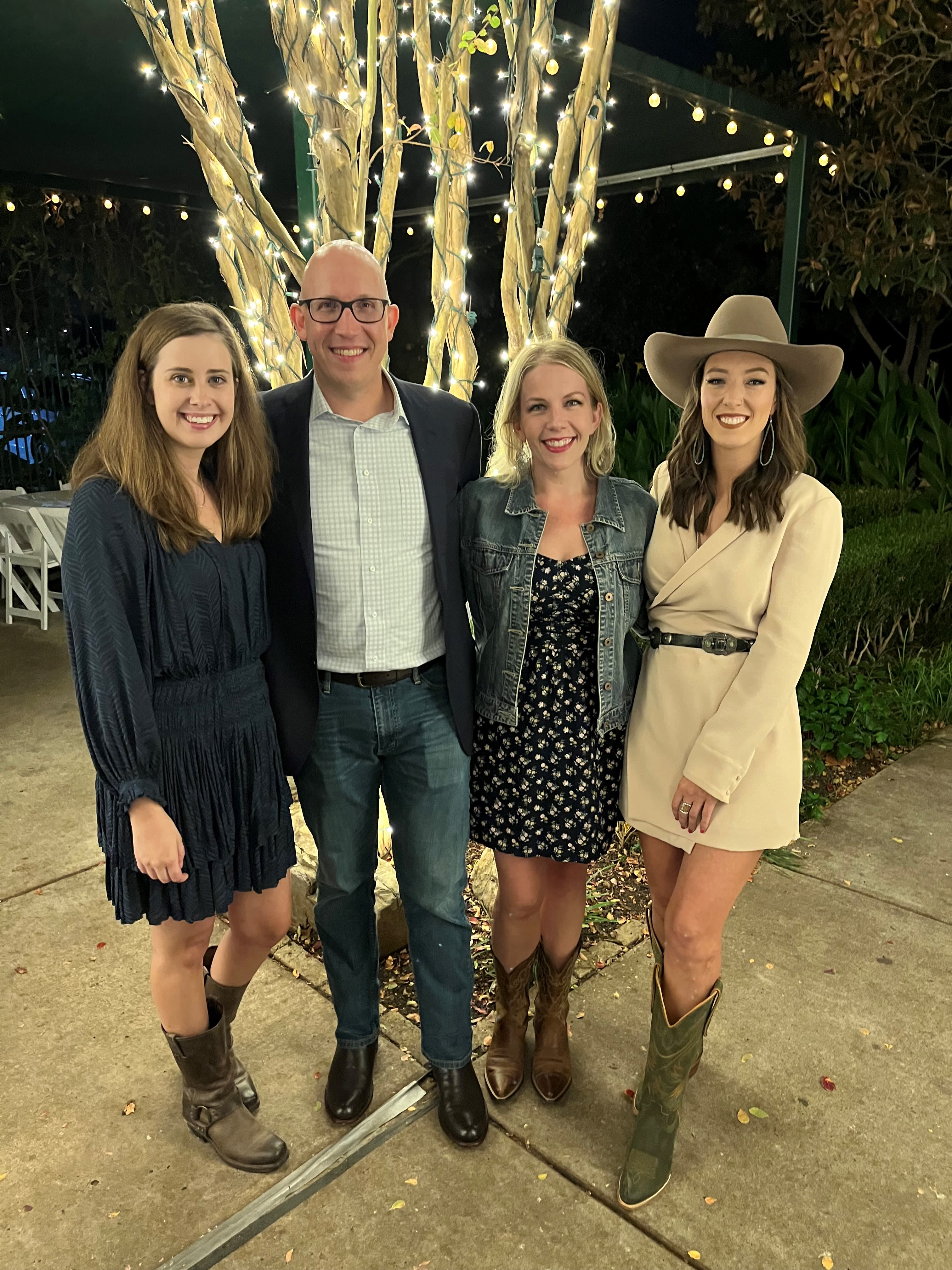 Four people posing together on an outdoor patio underneath string lights. 